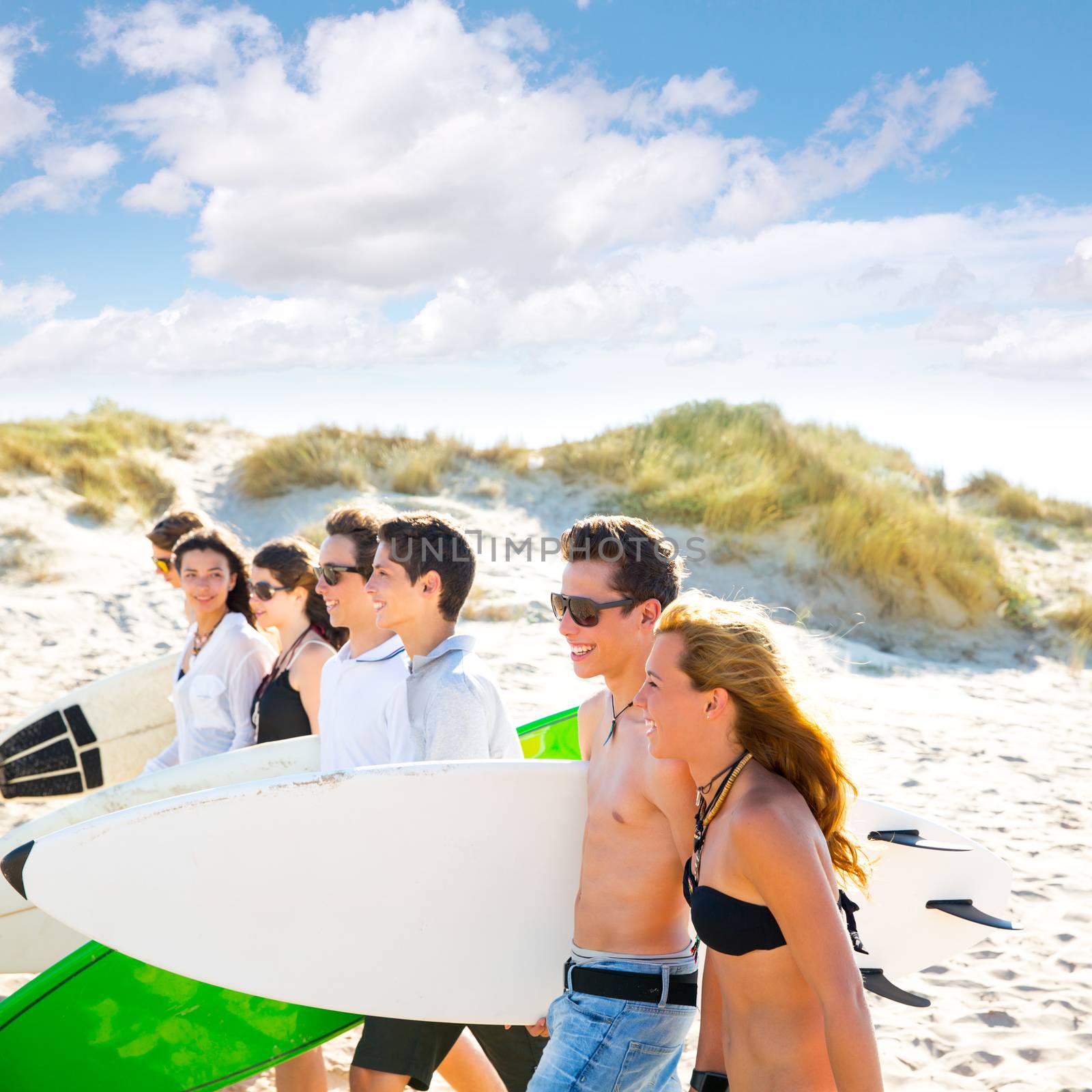Surfer teen boys and girls group walking on beach by lunamarina