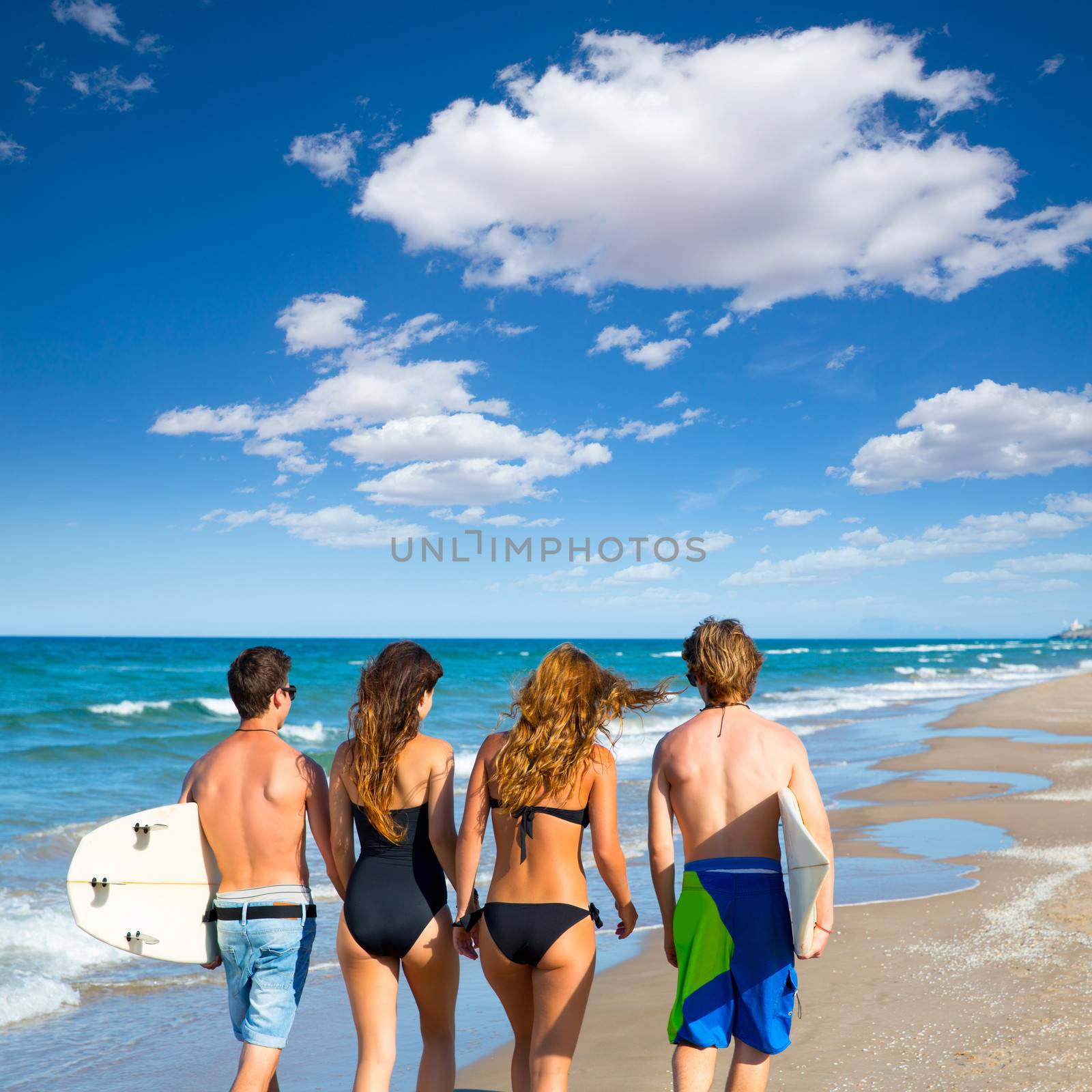 Teen surfers group of boys and girls walking rear view on beach