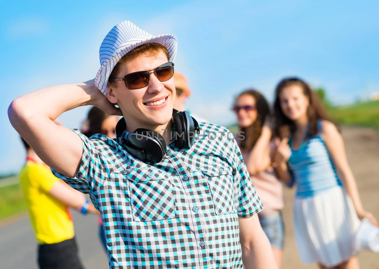 young man in sunglasses, a hat holds a hand on a background of blue sky and friends