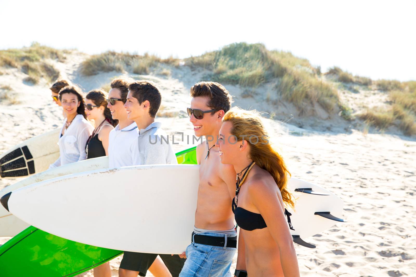 Surfer teen boys and girls group walking on beach sand