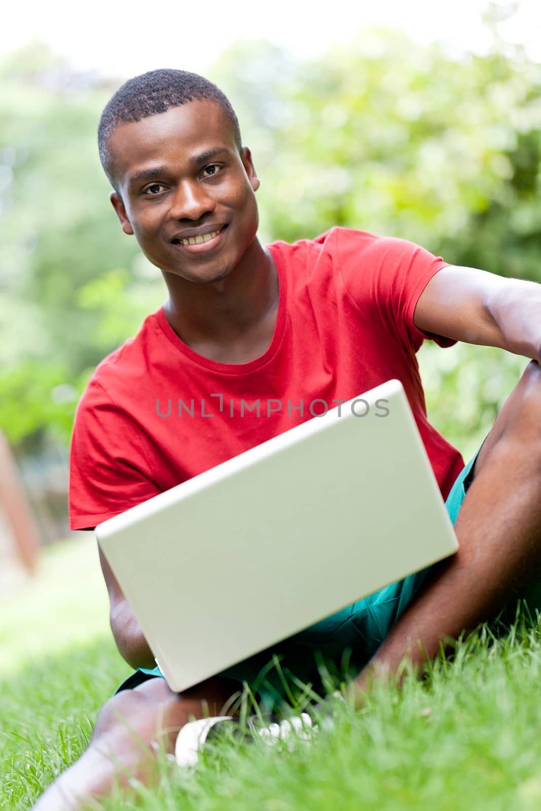 young smiling african student sitting in grass with notebook outdoor in summer man