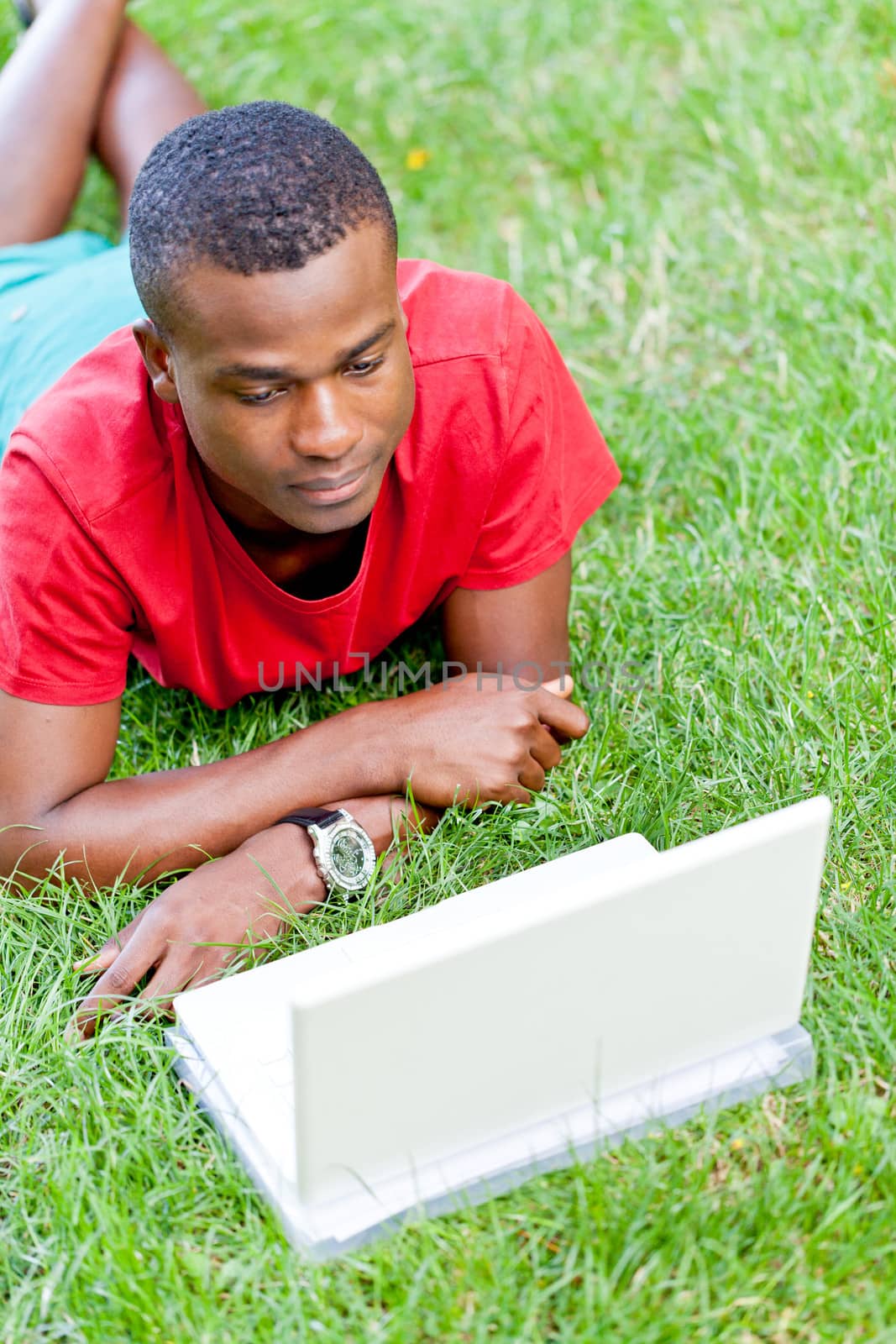 young smiling african student sitting in grass with notebook outdoor in summer man