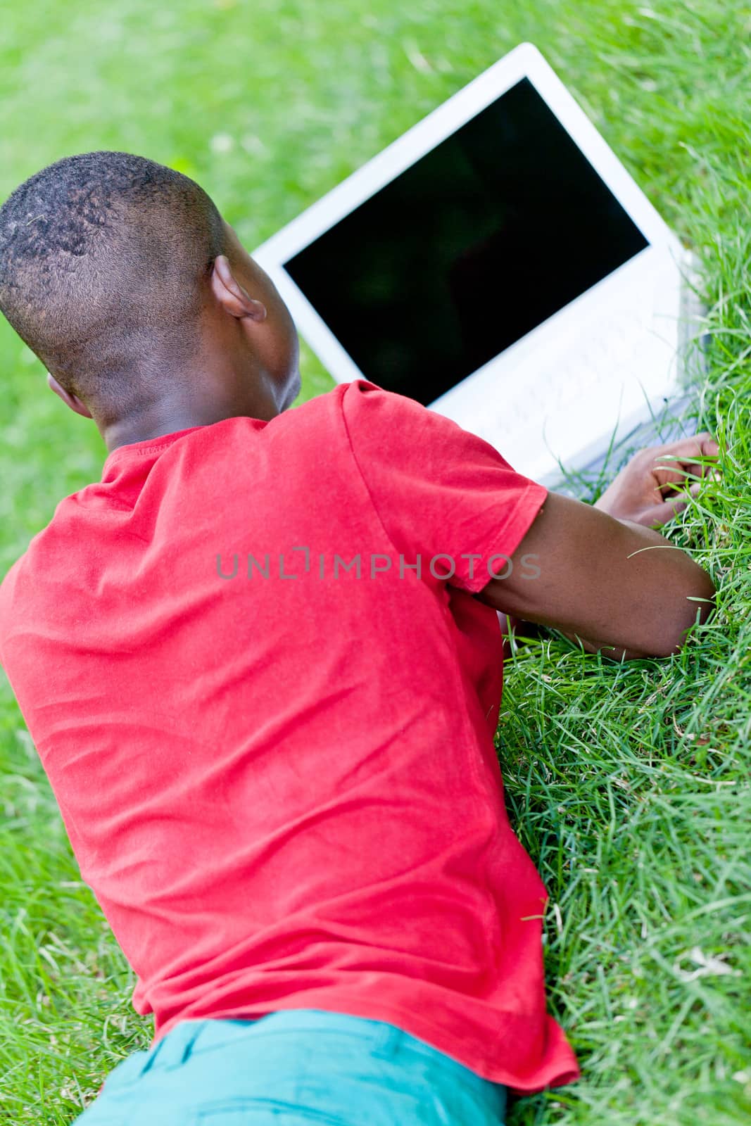 young smiling african student sitting in grass with notebook outdoor in summer man