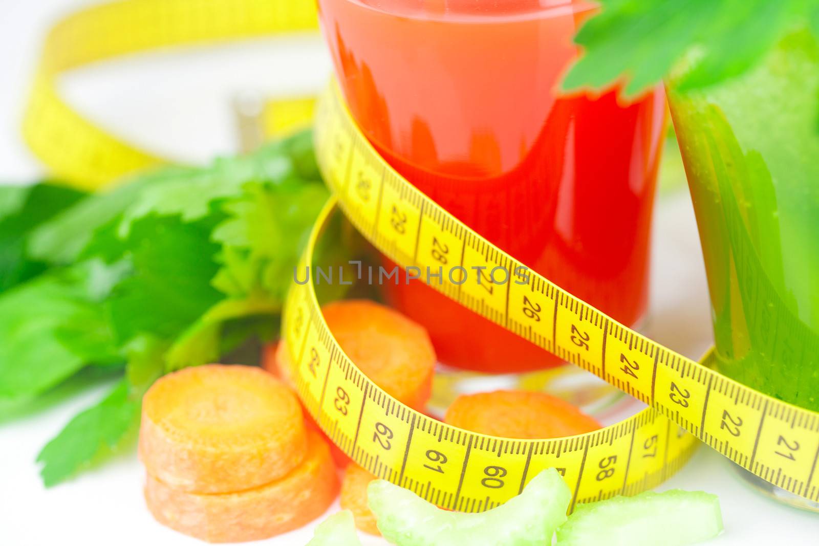 measuring tape, glass of celery juice and glass of carrot juice 