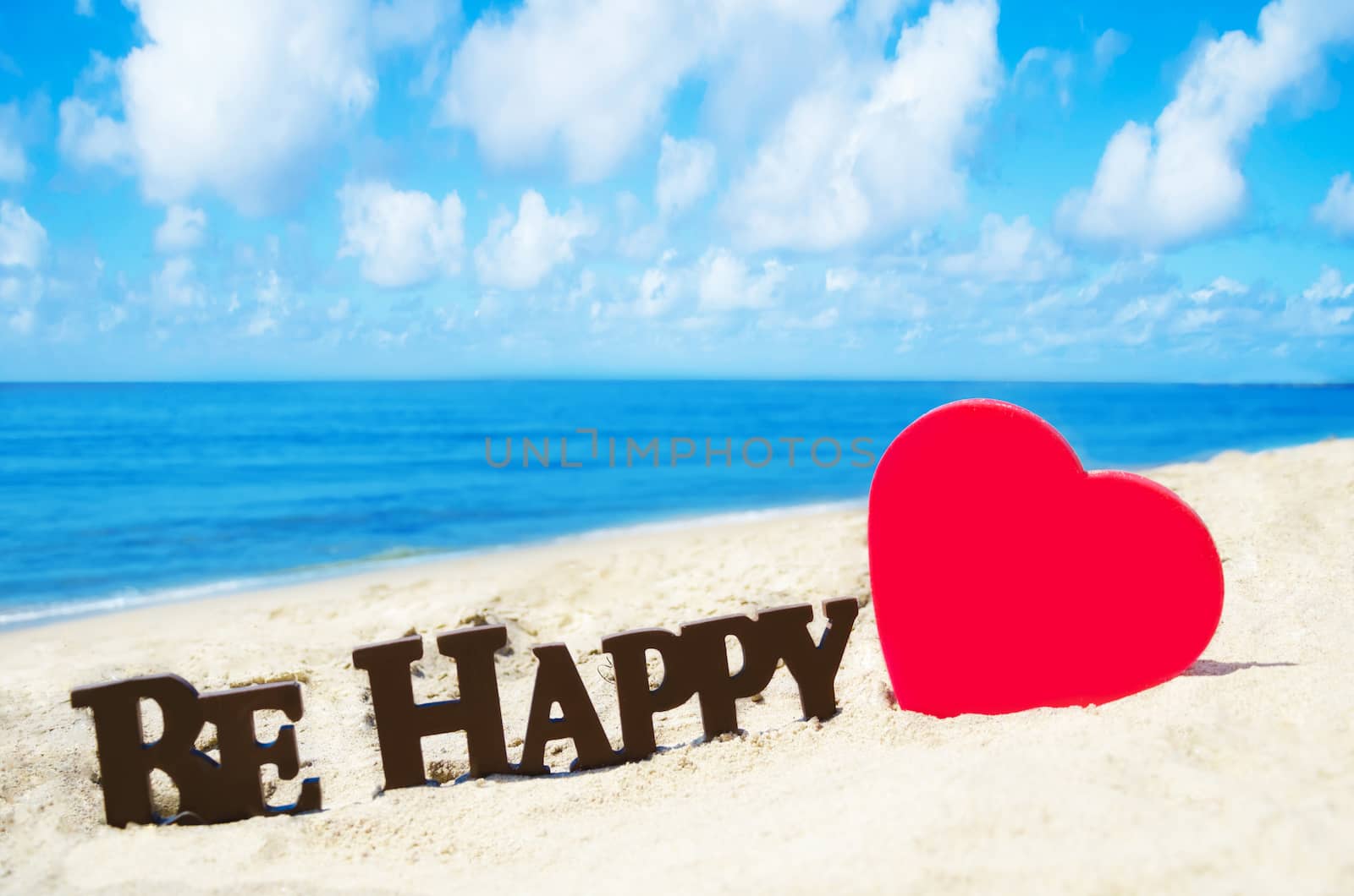 Sign "Be Happy" and heart shape on the sandy beach by the ocean in sunny day