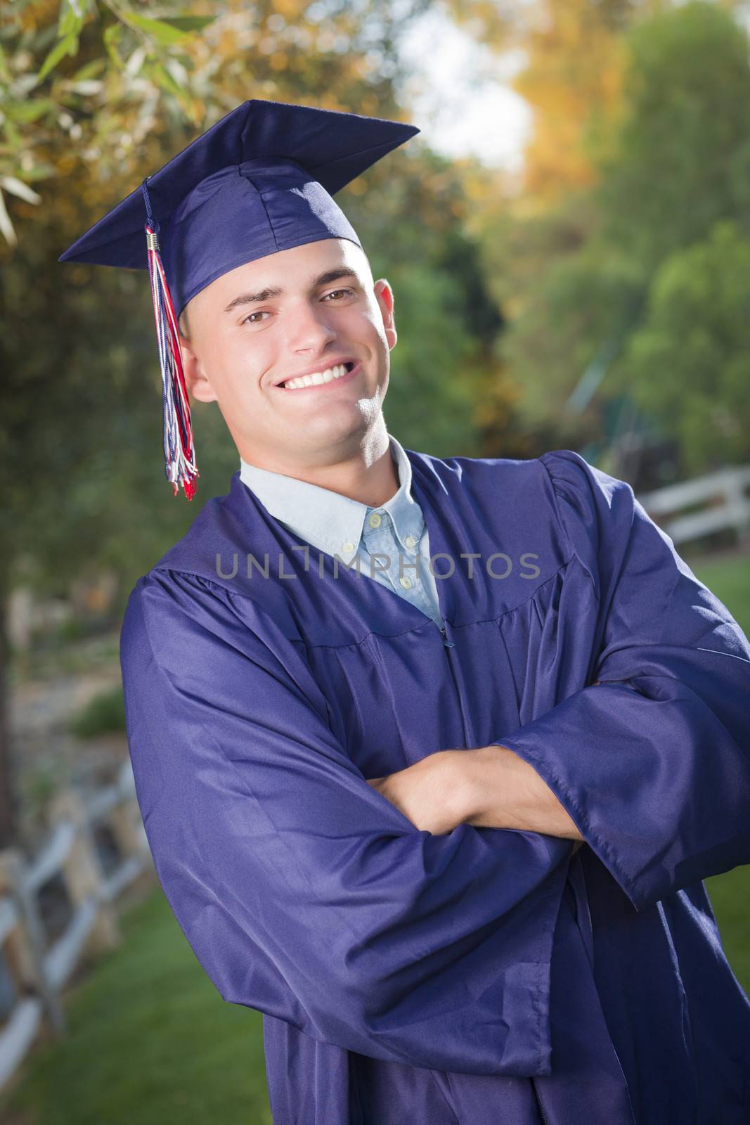 Happy Handsome Male Graduate in Cap and Gown Outside.