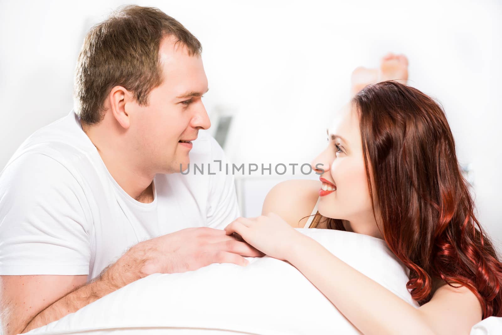 Young man and woman lying together in bed, smiling and happy