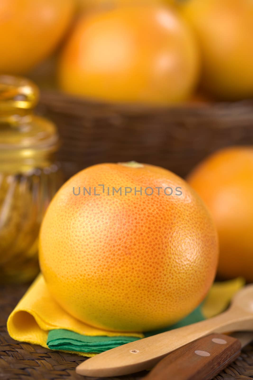Pink grapefruit on napkins with wooden spoon and knife on the side, sugar and basket in the back (Selective Focus, Focus on the front of the grapefruit)
