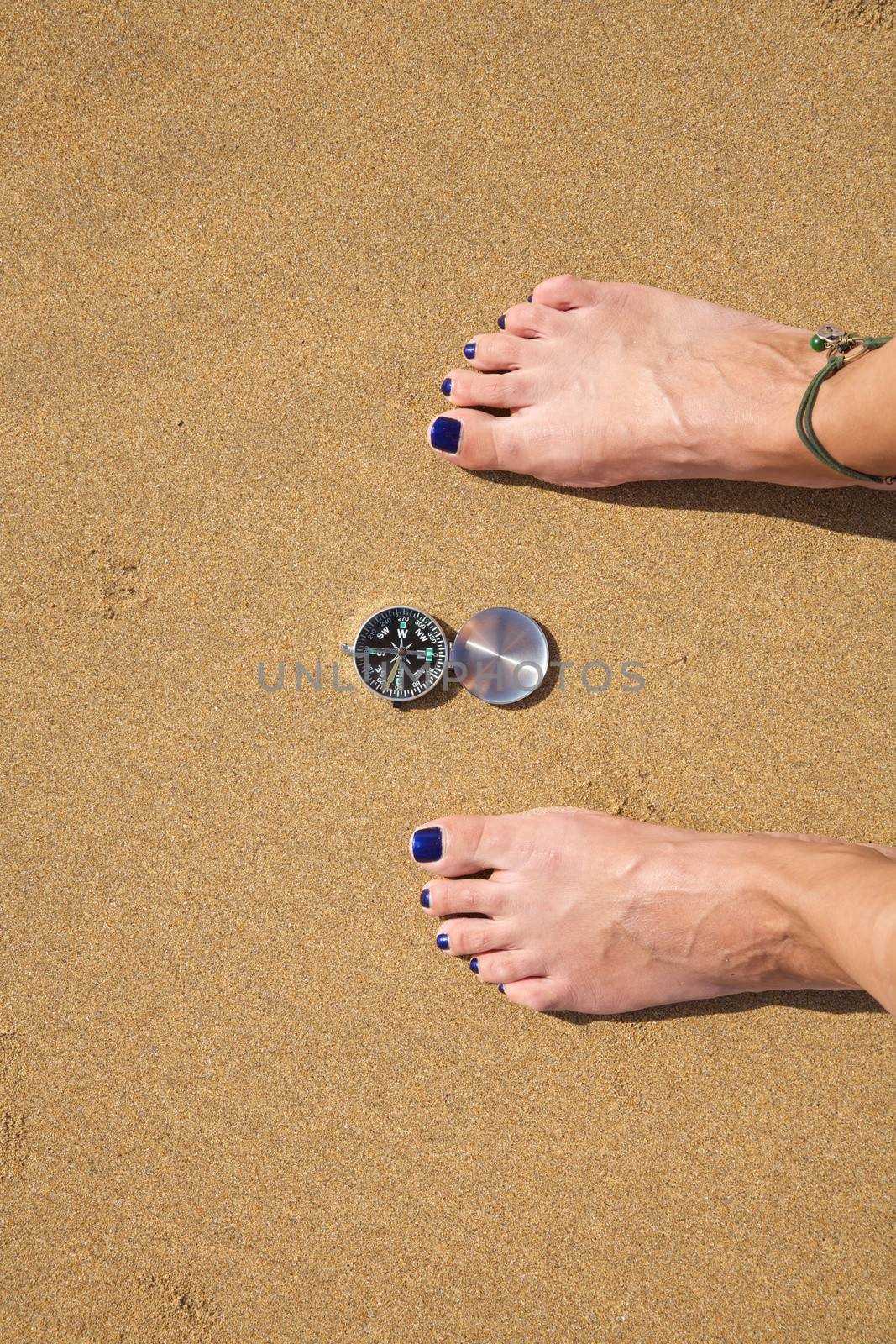 woman feet with a black and silver compass in a beach