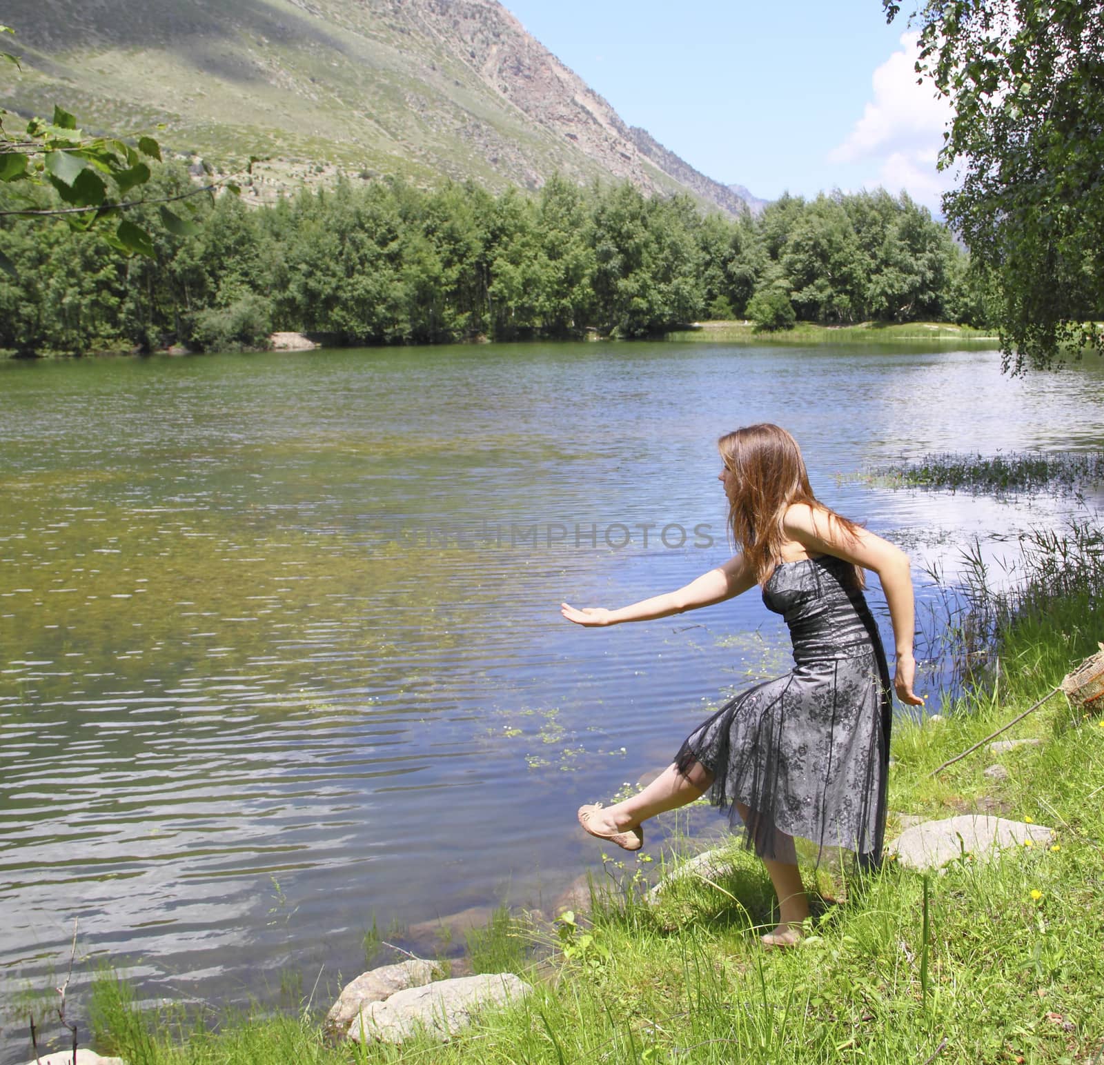 Young beautiful girl in a dress admires the mountain lake