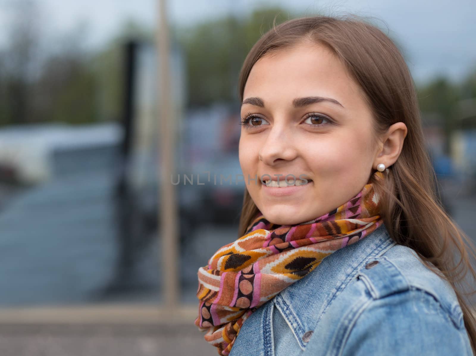 portrait of a beautiful girl in a denim jacket with a scarf on the street