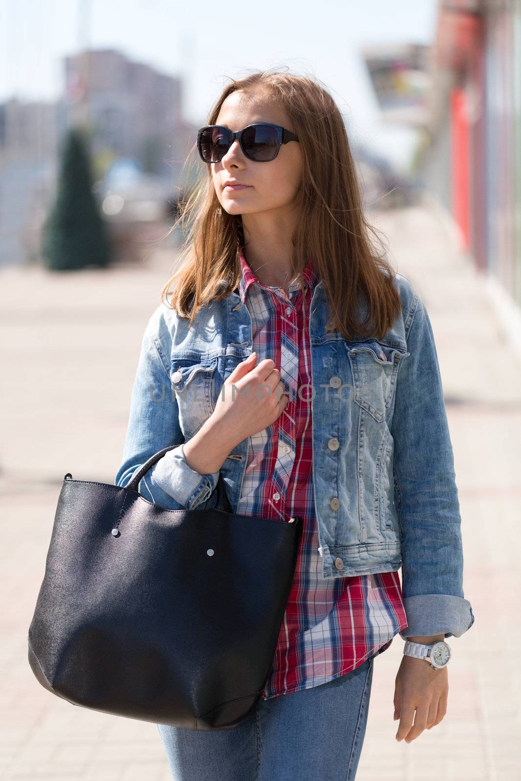 Young beautiful stylish girl in sunglasses and with a bag in hand on a sunny day on the streets of major cities