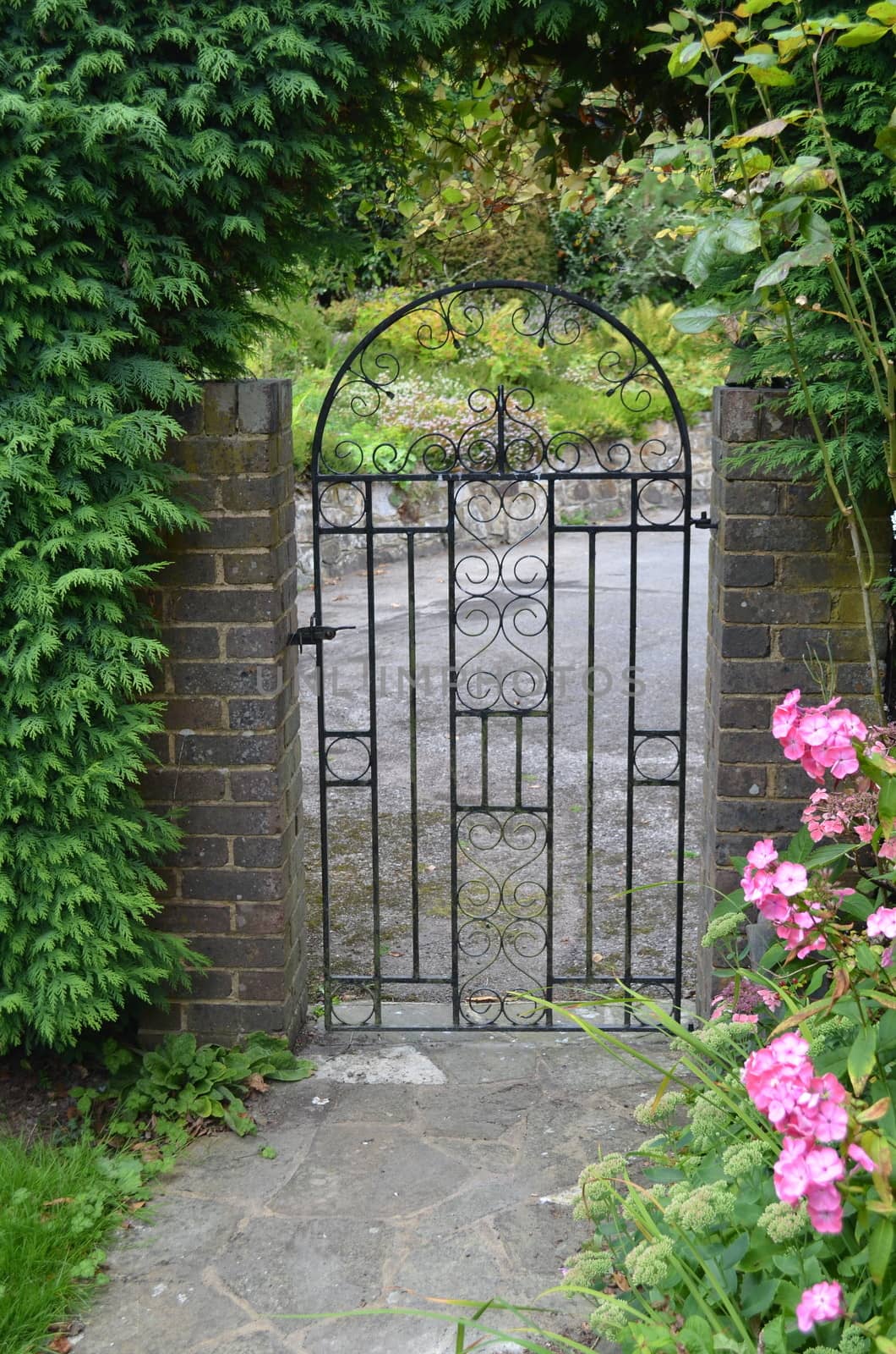 Iron gate at a private home with flowers and brick surround.