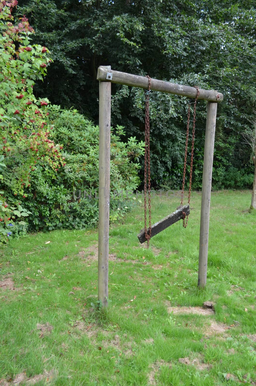 Old wooden play swing in garden setting.