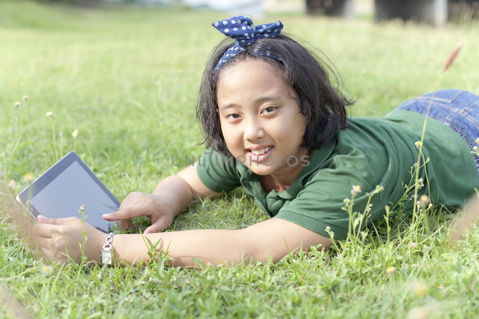 girl lying on green grass with computer tablet in hand use for technology theme