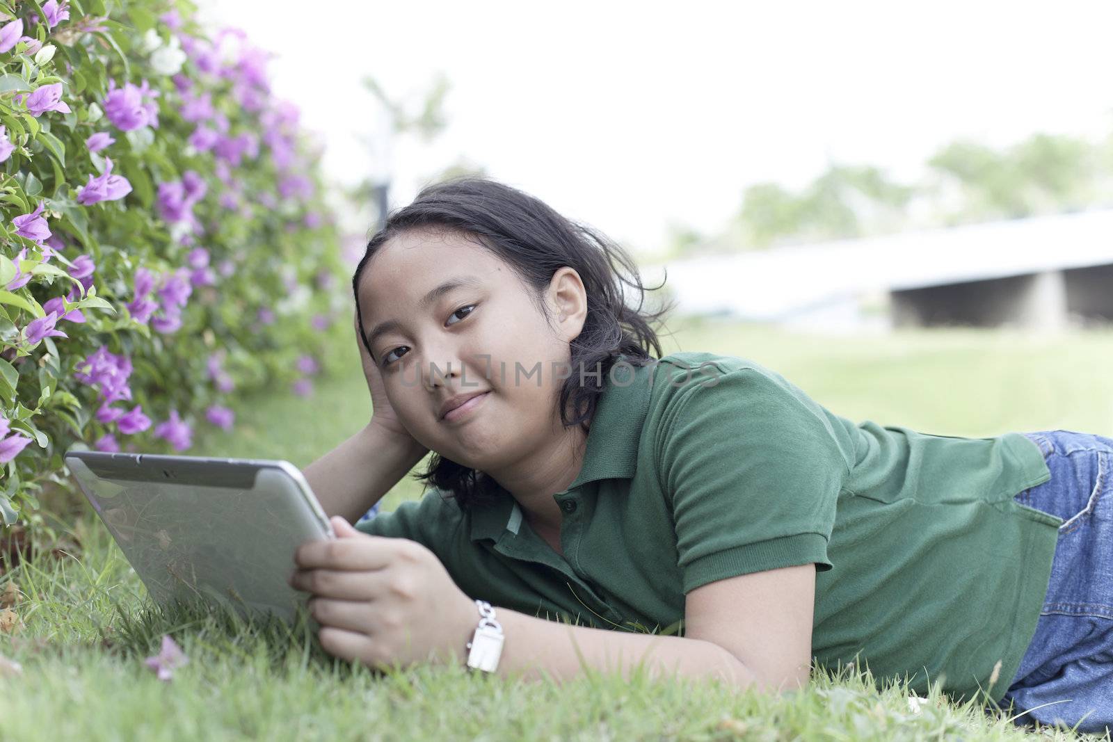 girl and tablet computer lying on green grass field use for high tech communication theme