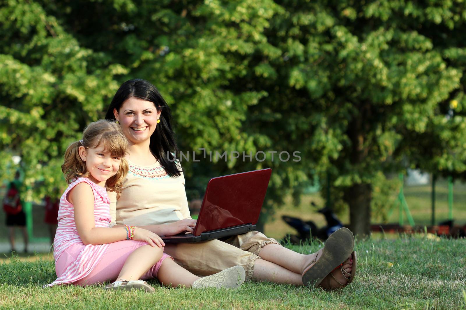 happy little girl and woman with laptop in park