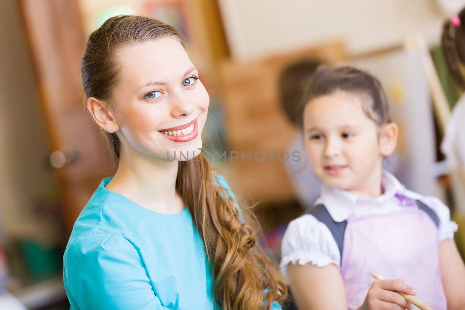 Little girl painting with teacher at kindergarten