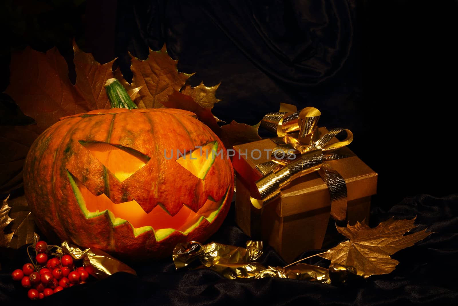 Halloween pumpkin with autumn leafs and gift on black