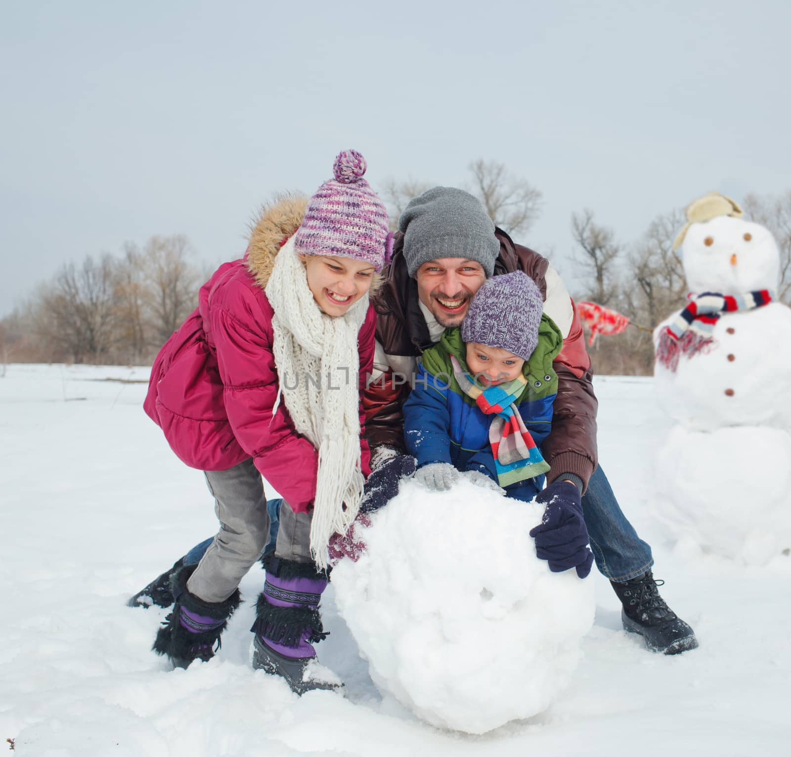 Happy beautiful children with father building snowman outside in winter time