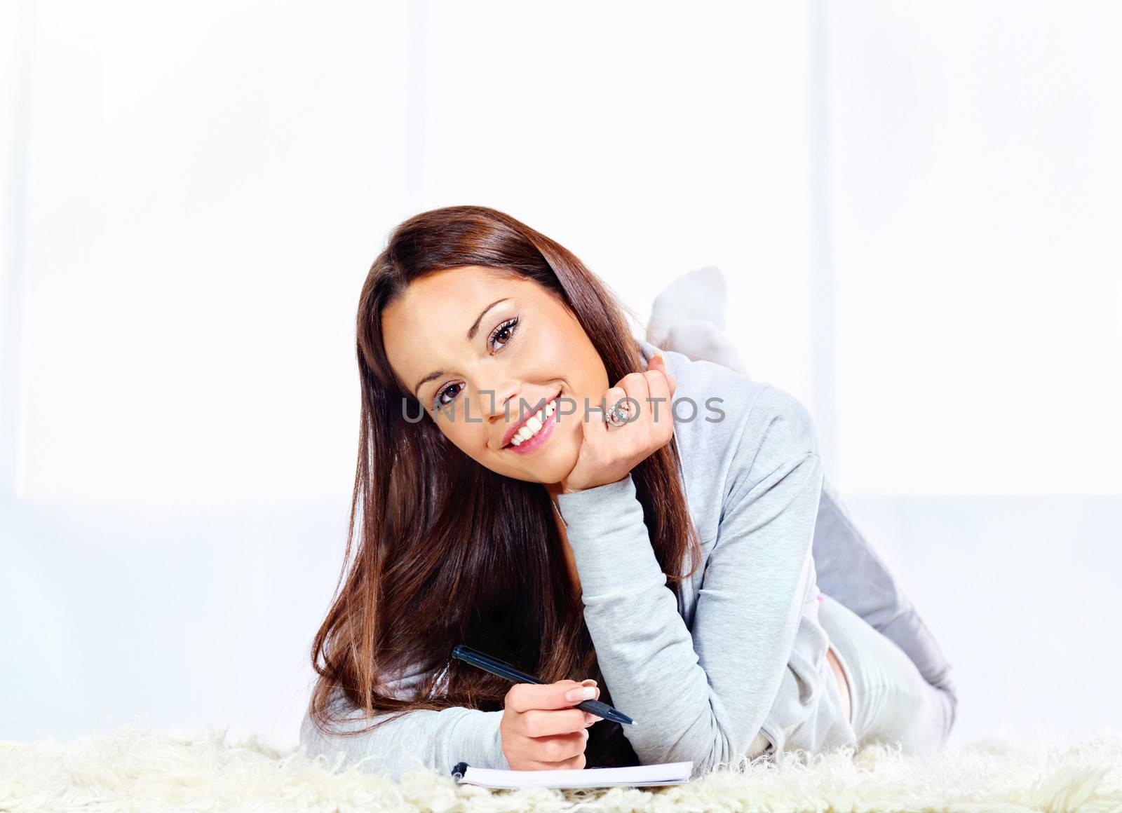 Young smiled woman on carpet at home with notepad and pen