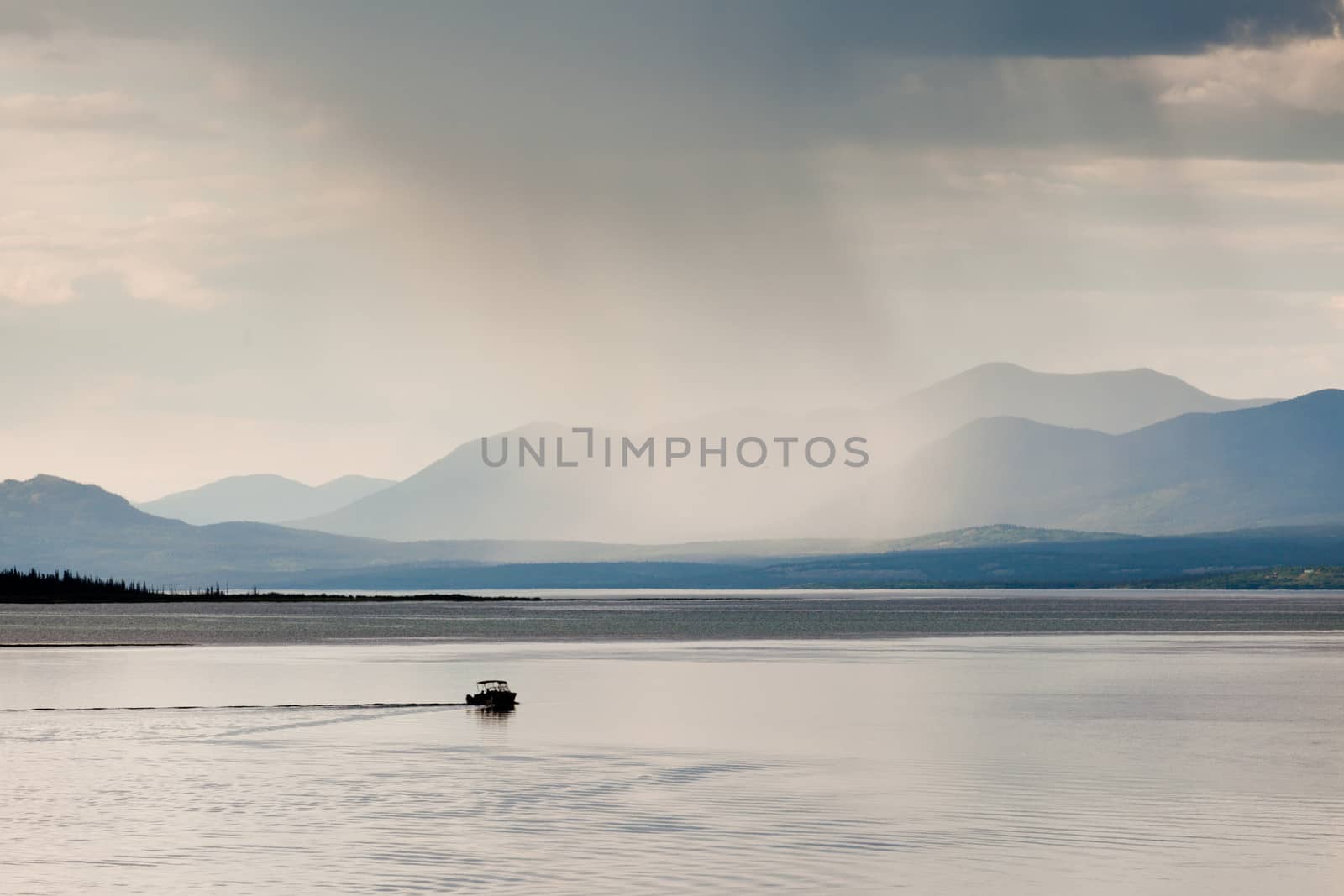 Heavy rain shower over Marsh Lake Yukon Territory Canada and distant mountain range with a small motorboat out on tranquil water