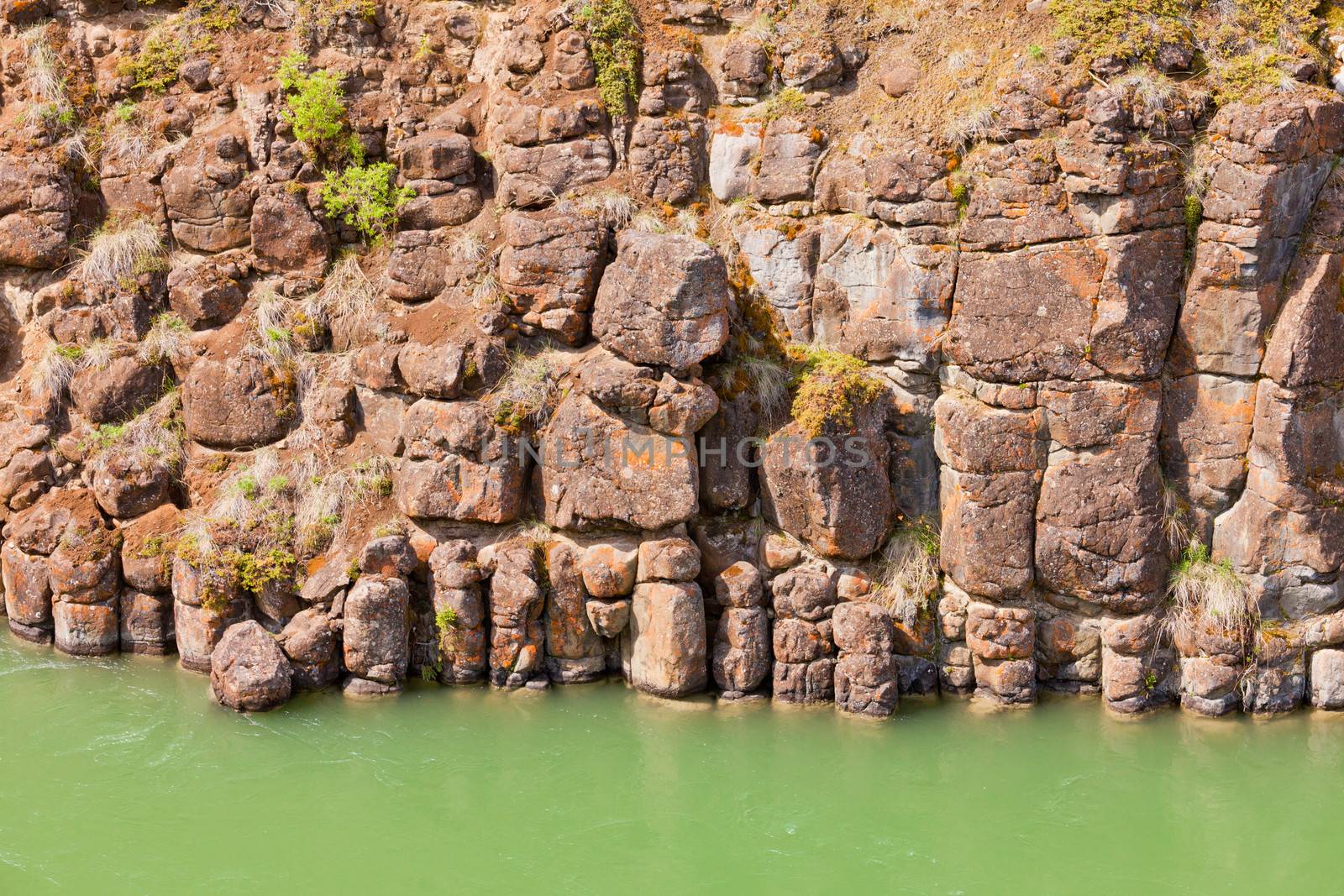Close-up of weathered geologic basalt rock cliff wall of Miles Canyon with water of Yukon River  Yukon Territory  Canada