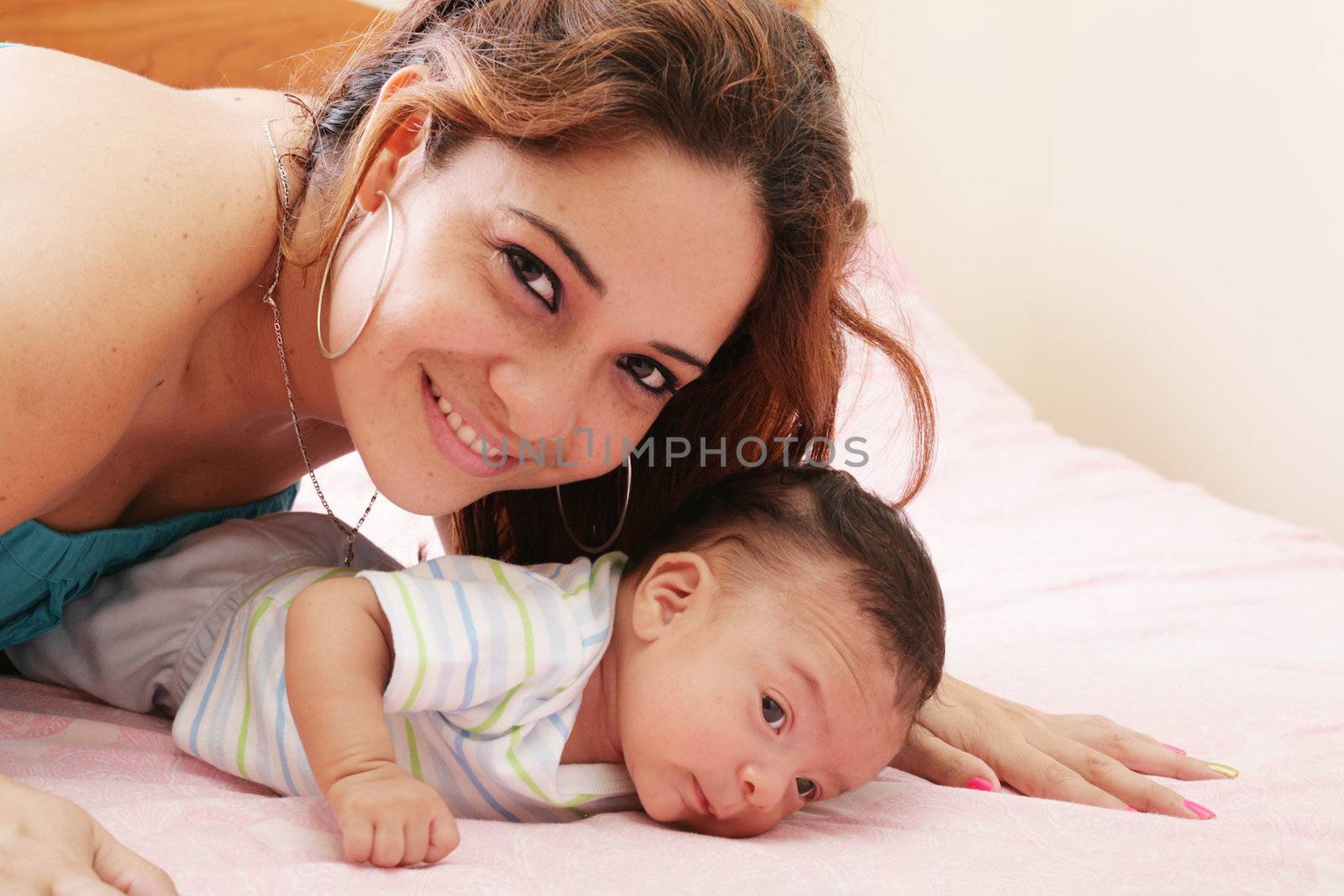 Hispanic mom lying down on bed and holding her infant son