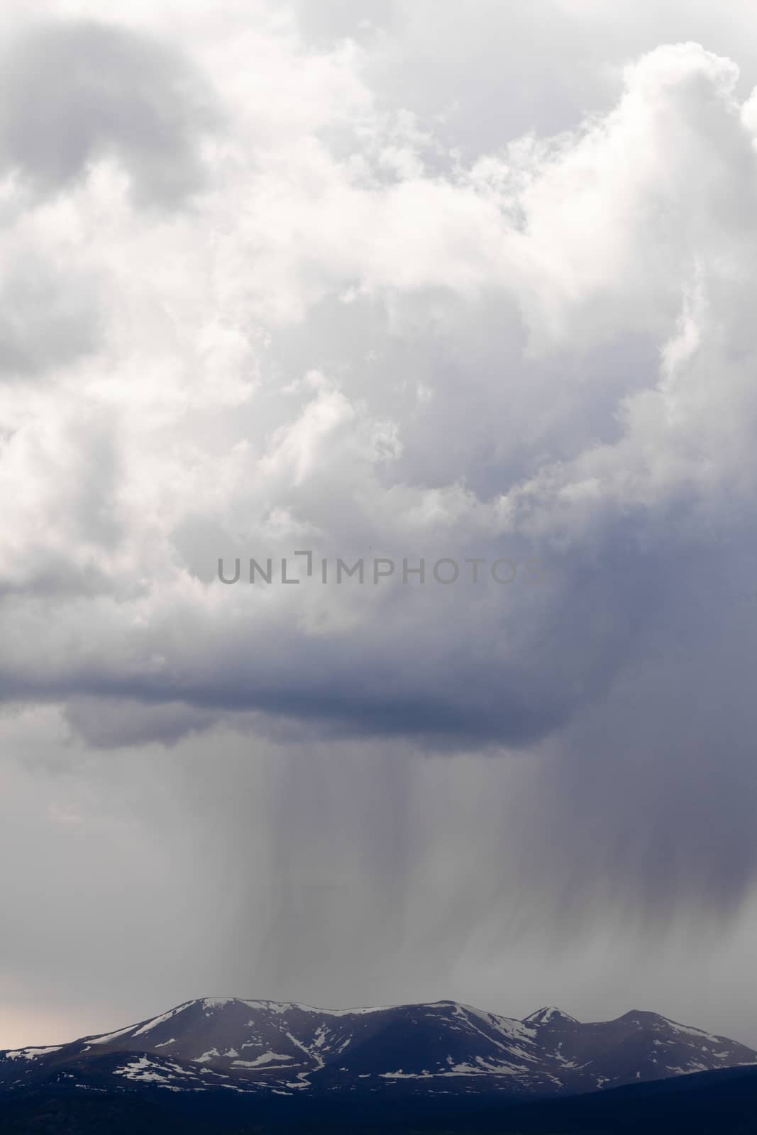 Dramatic rain storm cumulonimbus cloud formation bringing bad weather towering over snowy mountains in Yukon Territory Canada