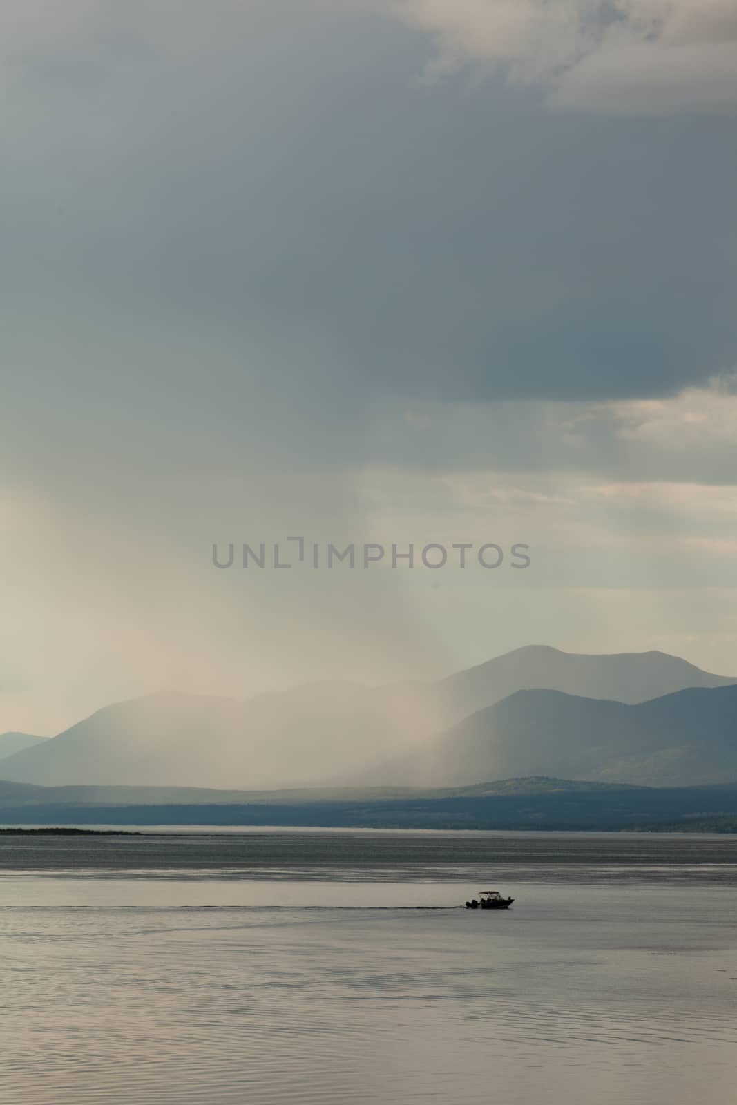 Heavy rain shower over Marsh Lake Yukon Territory Canada and distant mountain range with a small motorboat out on tranquil water