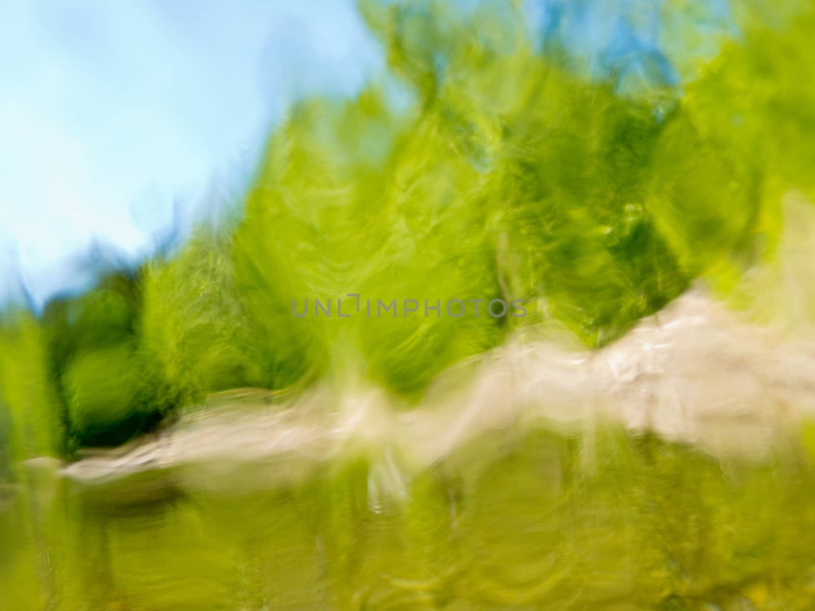 Blurry nature background texture pattern with blurred wavy distortions of springtime forest lake shore and sunny blue sky