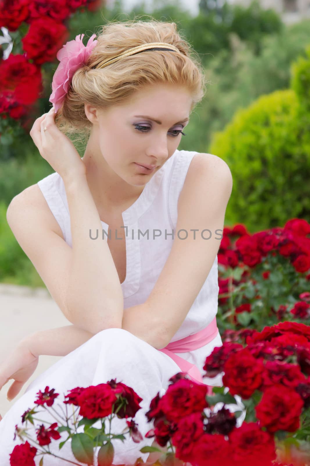 Sensual woman sitting among pink rose garden