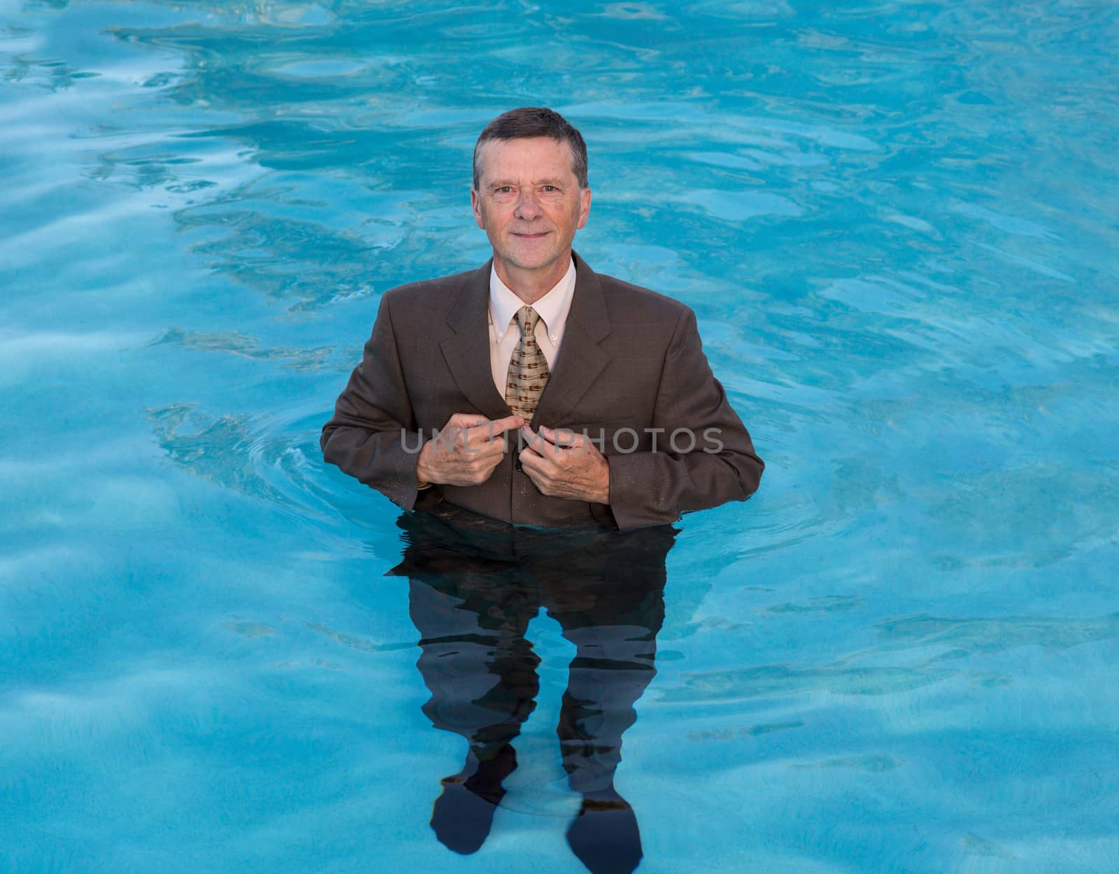 Senior caucasian businessman in suit up to waist in deep blue water and smiling at the camera