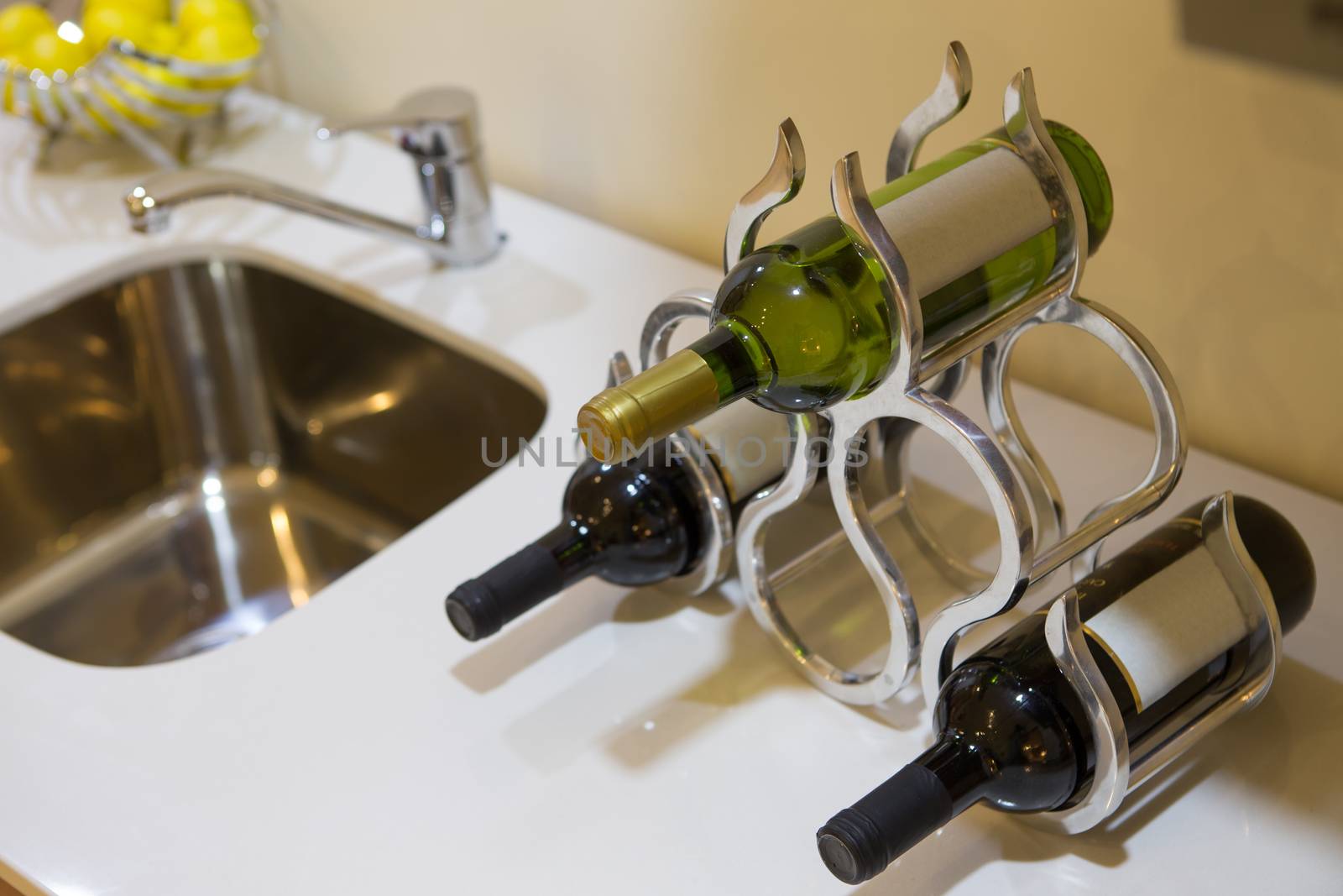 Three bottles of wine with blank labels in a stylish wine rack on a kitchen or bar counter alongside a sink