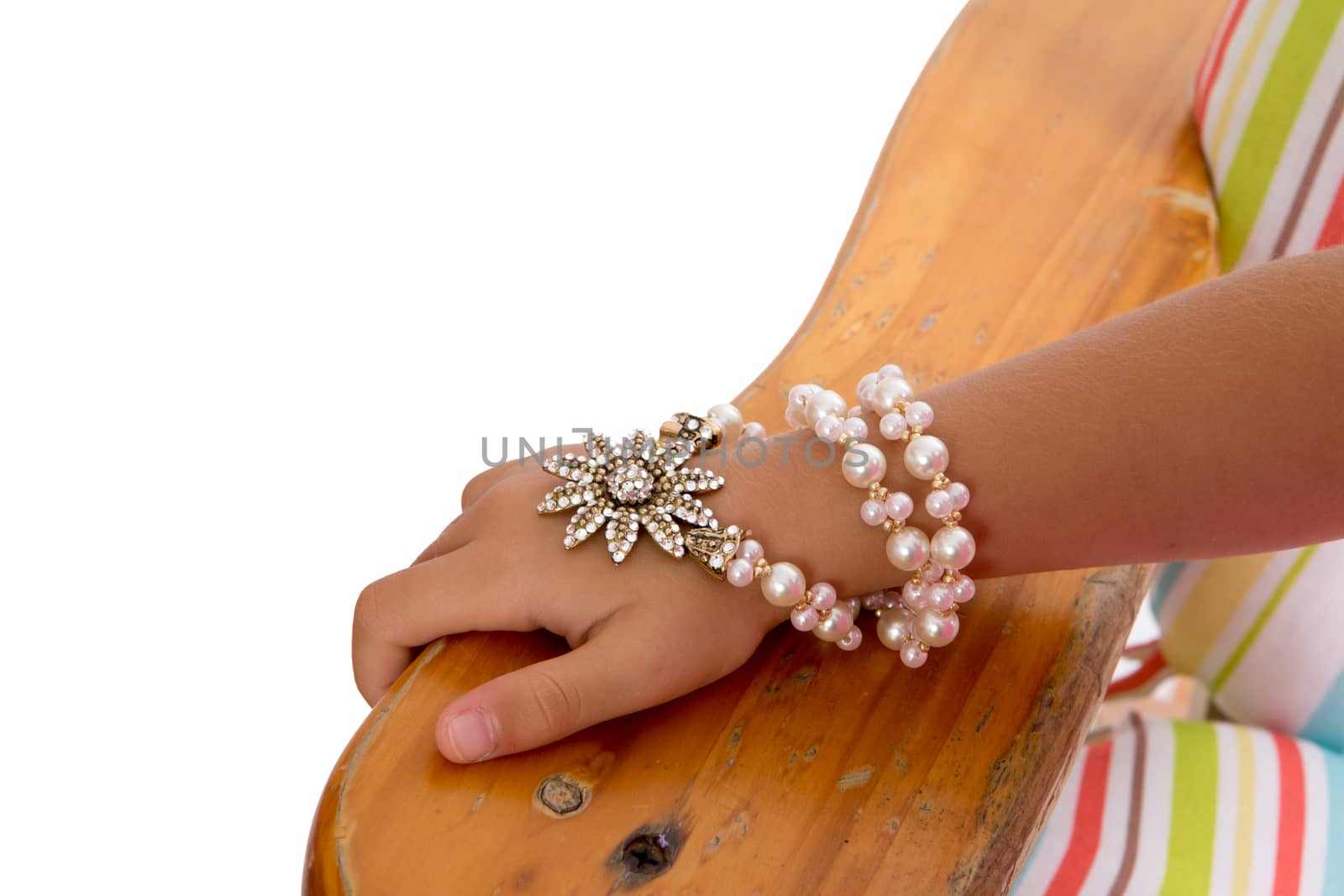 Young girl wearing a pearl and foral bracelet entwined several times around her wrist, close up view of her hand resting on the arm of a wooden chair