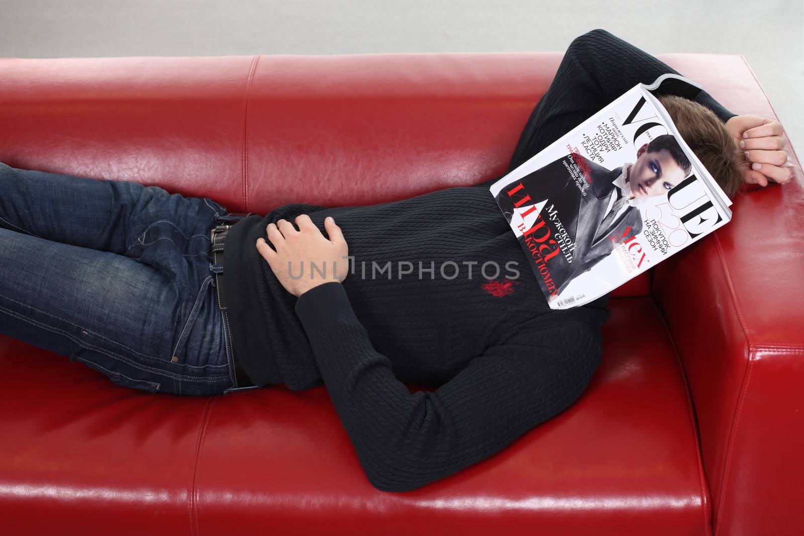 young man with magazine sitting on sofa by andersonrise