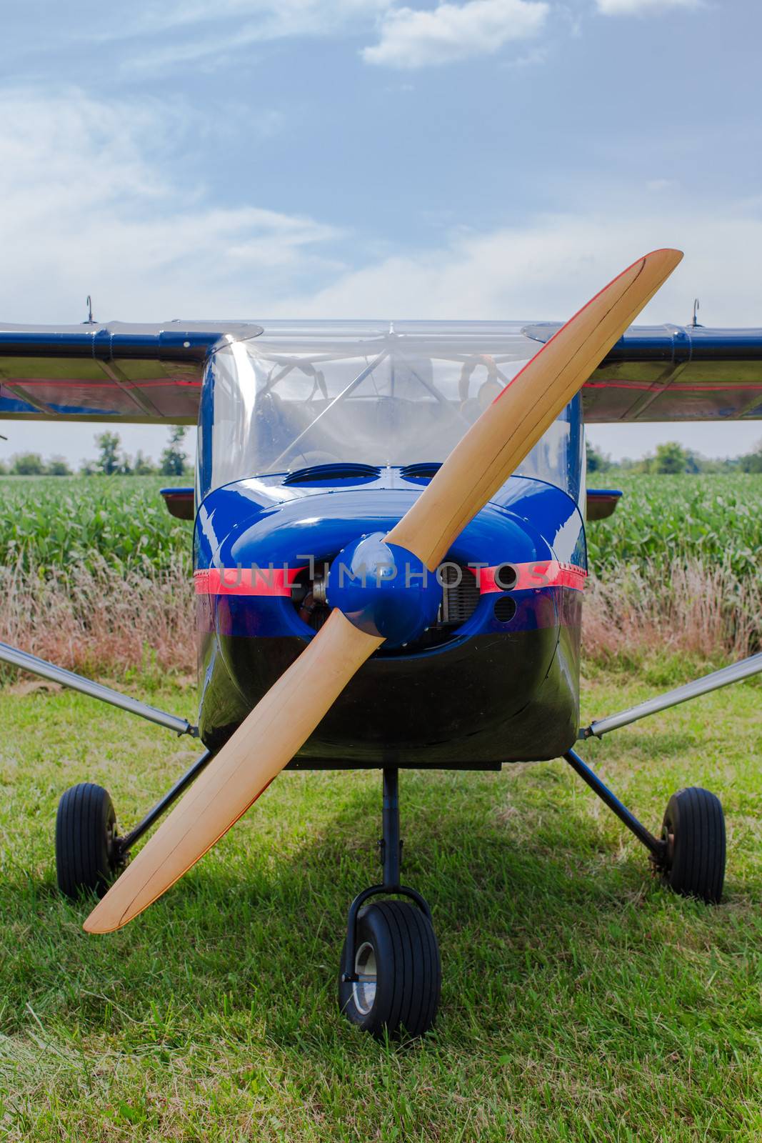 Propeller and nose of a blue single engine fixed wing aircraft parked in a rural field , closeup view