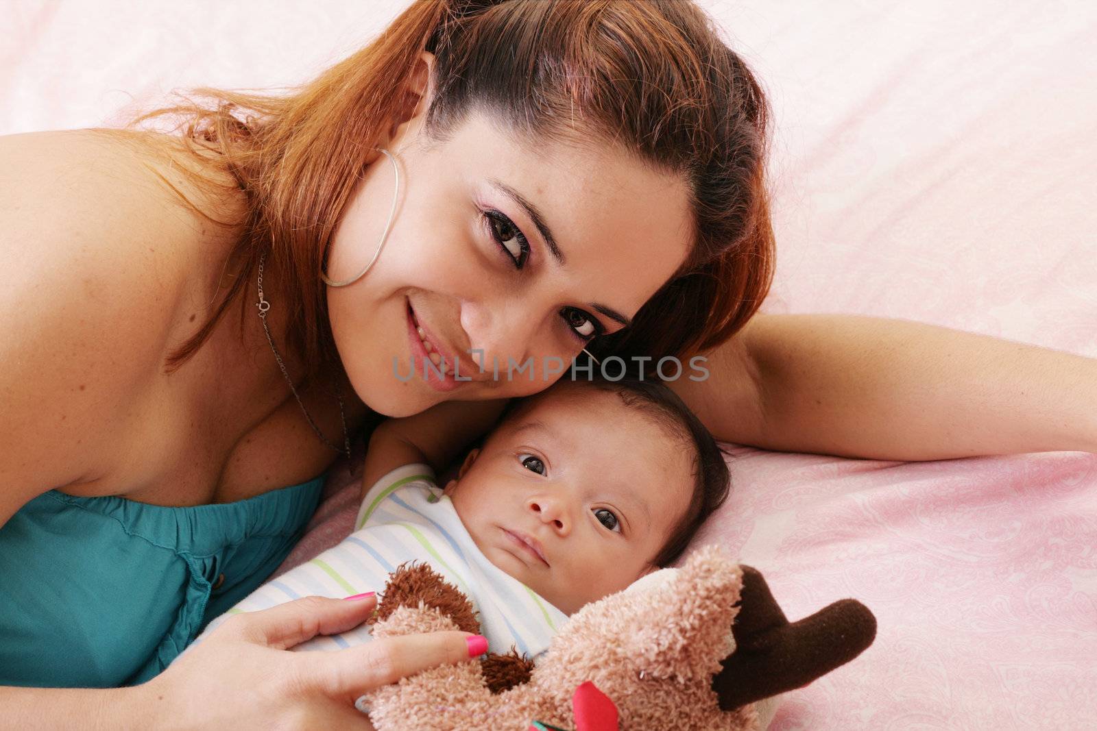Happy mum and baby boy smiling in the bed holding teddy bear