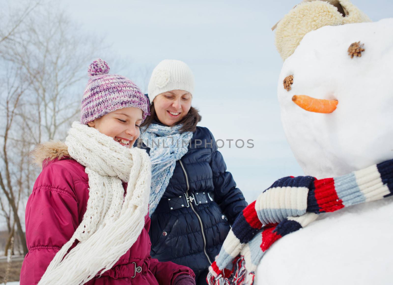 Happy beautiful girl with mother building snowman outside in winter time