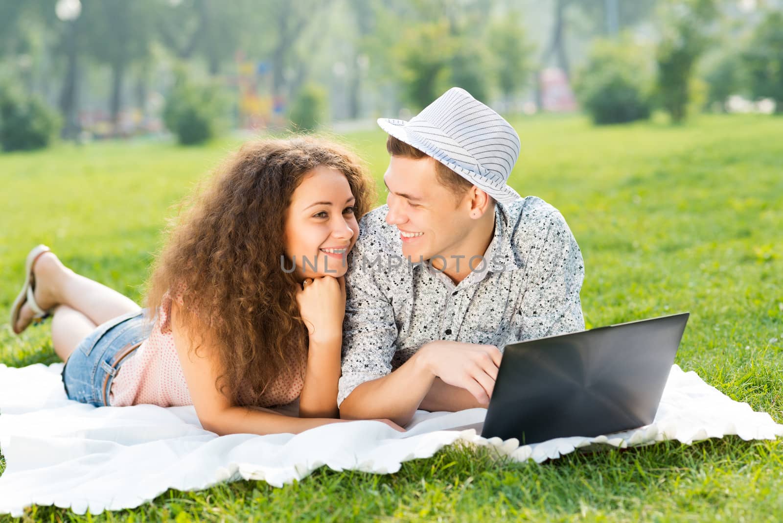 couple lying together in a park, working together on a laptop