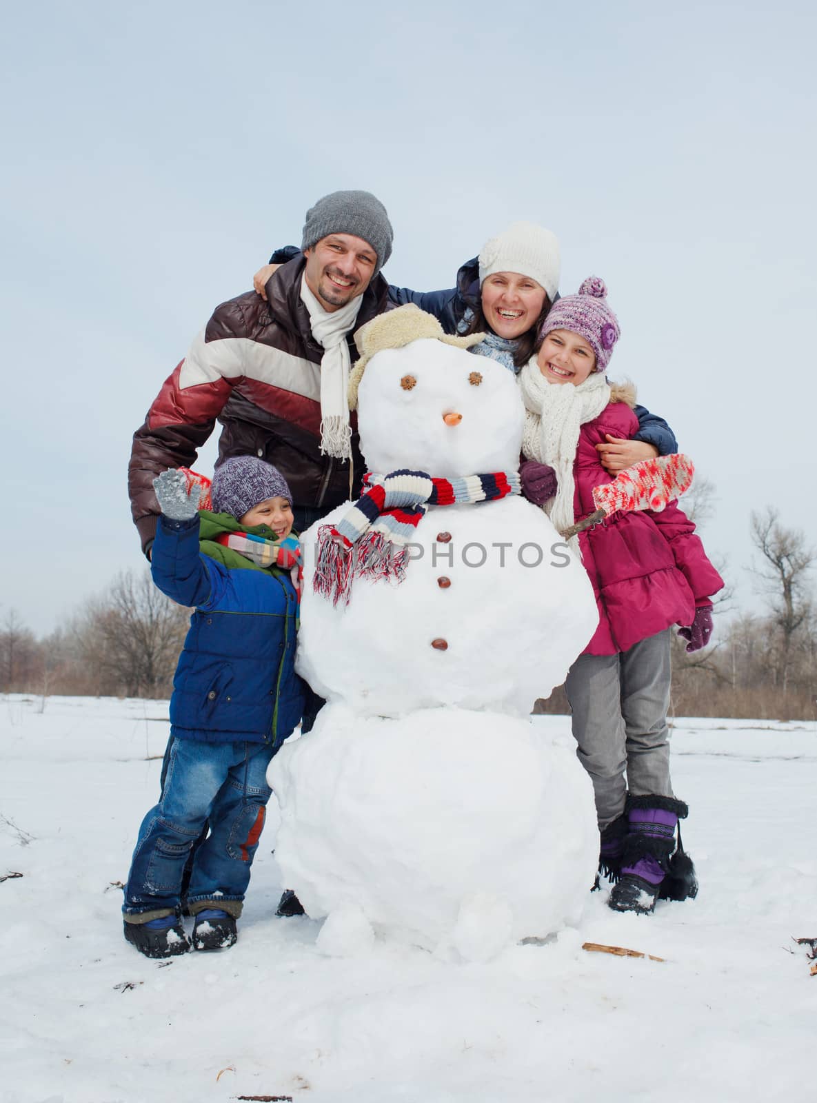 Happy beautiful family with two kids building snowman outside in winter time