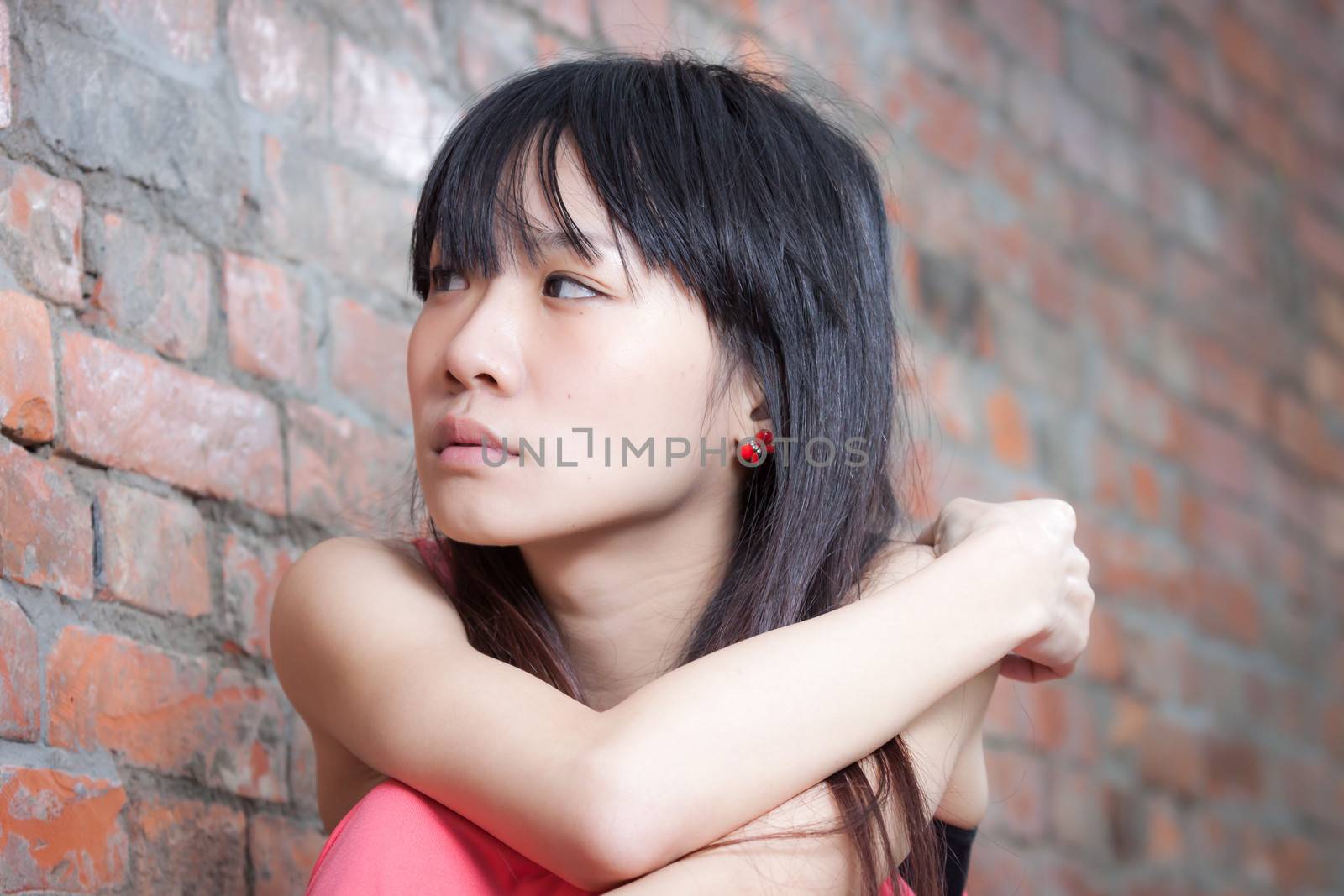 Young Asian woman sitting by red brick wall feeling depressed and sad
