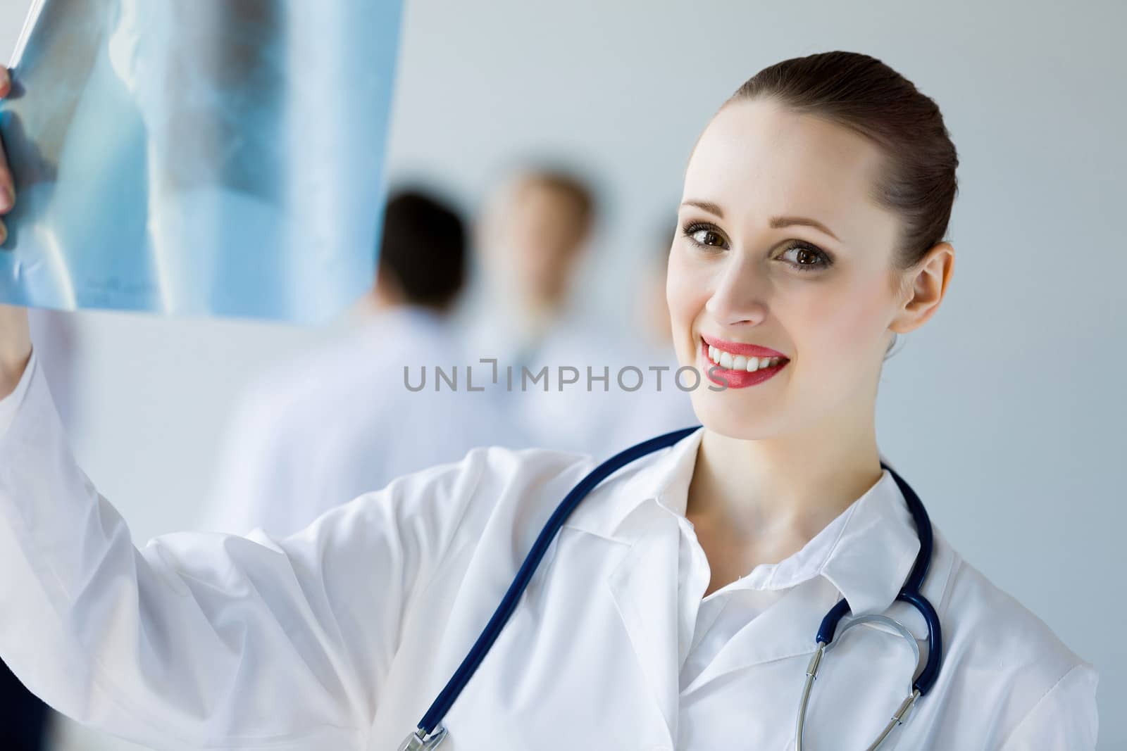 Attractive female doctor in white uniform with colleagues at background