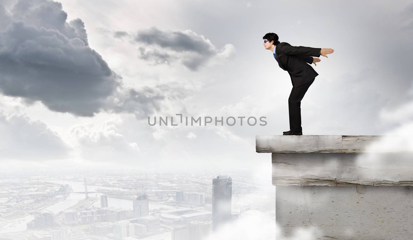 Image of young businessman in goggles jumping from top of building