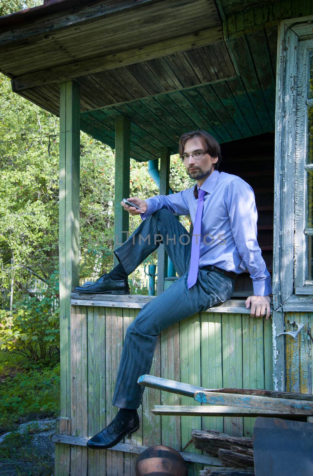 business man in glasses holding a phone while sitting on the porch