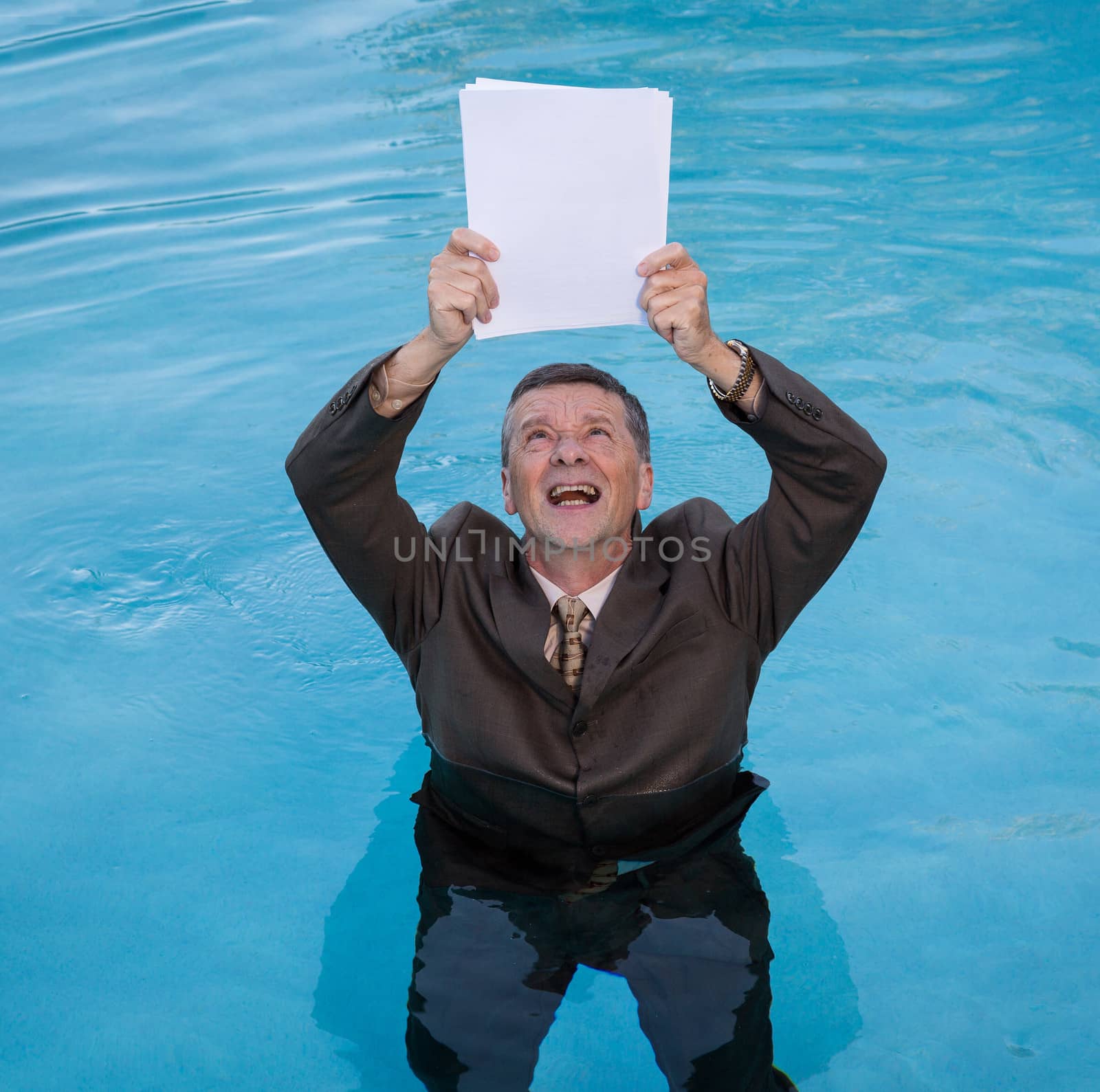 Senior caucasian businessman in suit up to waist in deep blue water worried about drowning in paperwork and holding blank document