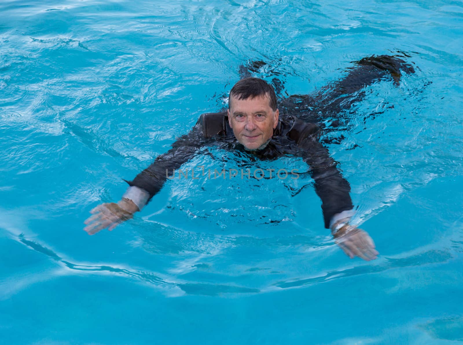 Senior caucasian businessman in suit swimming in deep blue water and smiling as he tries to keep afloat