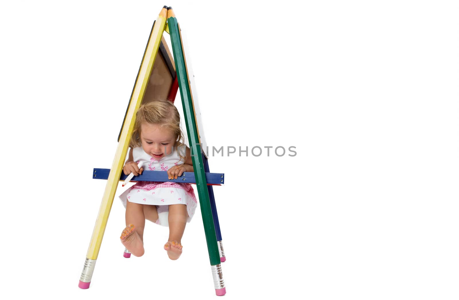 Small barefoot girl having fun swinging on a signboard, hanging on the cross bar with her feet in the air, isolated on white