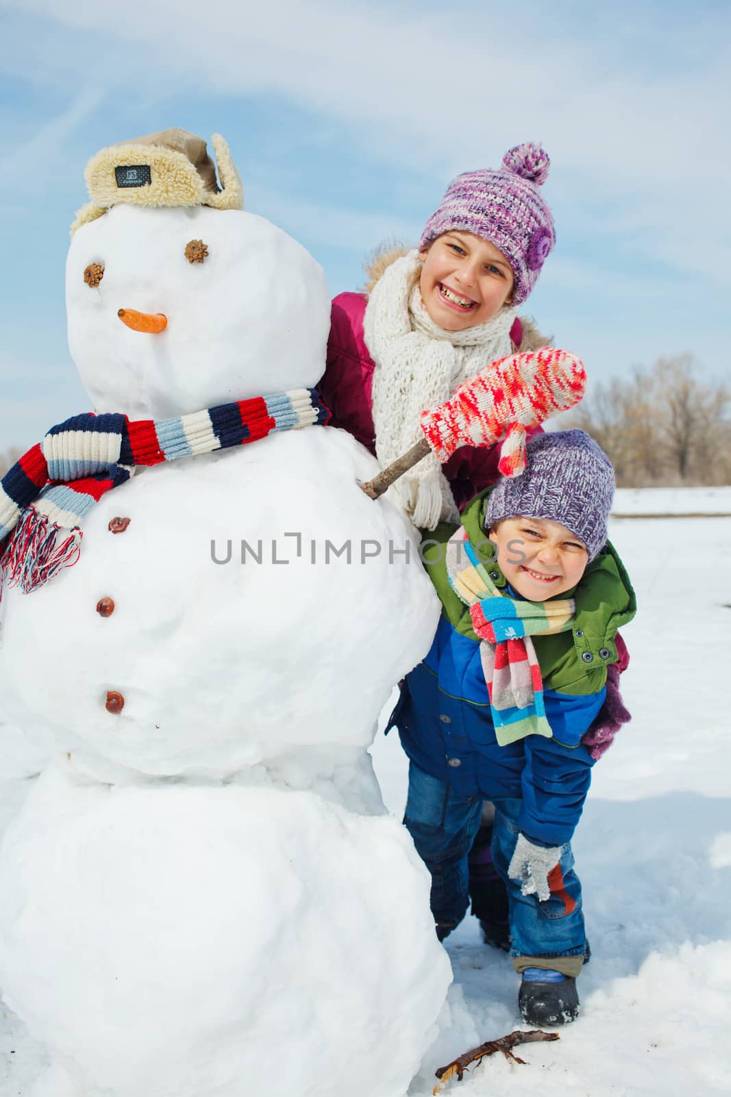 Happy beautiful children with snowman outside in winter time