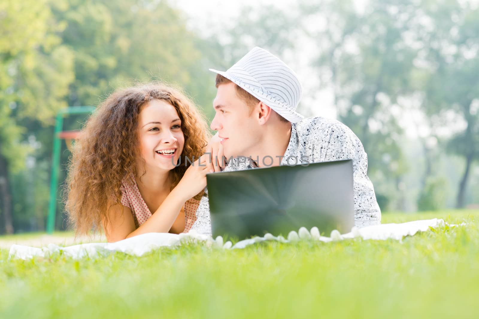 couple lying together in a park, working together on a laptop
